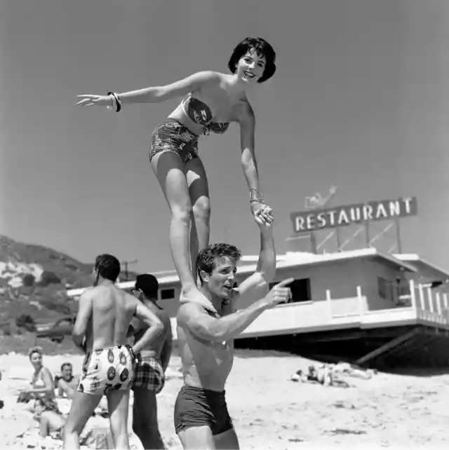 Here's Natalie Wood standing on the shoulders of actor Steve Rowland at the Thalians Beach Ball. (1956)